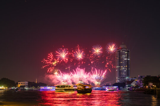 View of fireworks over the Chao Phraya River near the Memorial Bridge with illuminated river boats and city skyline at night in Bangkok, Bangkok, Thailand.