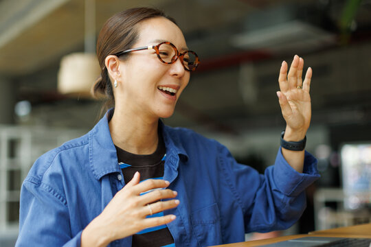 Smiling Asian businesswoman with glasses on a video call in a modern coworking space