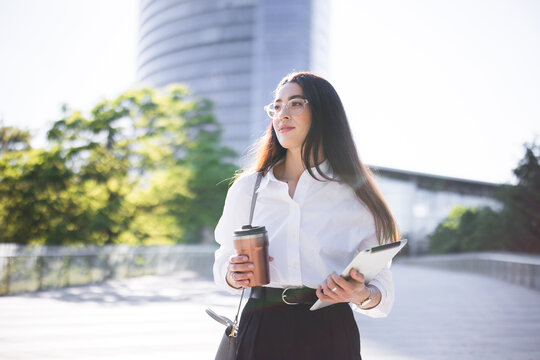 Businesswoman walks to work with a tablet and reusable coffee cup