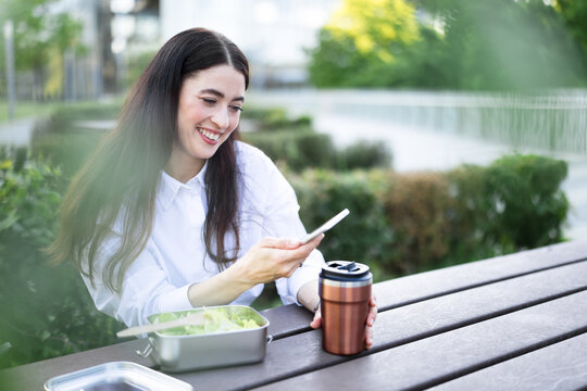 Smiling businesswoman uses smartphone during outdoor lunch break