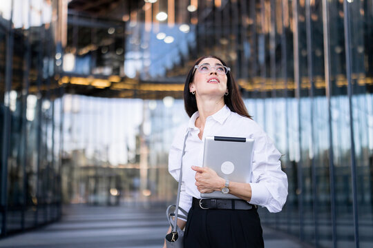 Confident businesswoman walks through urban office campus with tablet