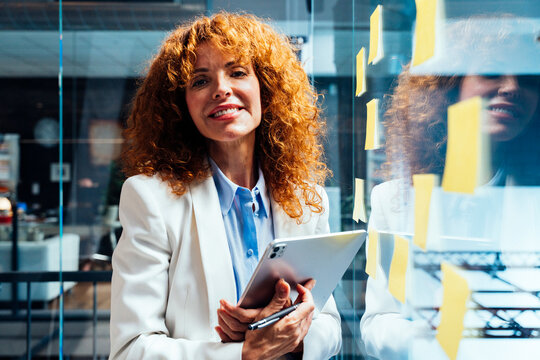 A smiling mature businesswoman holds a tablet at the corporate office
