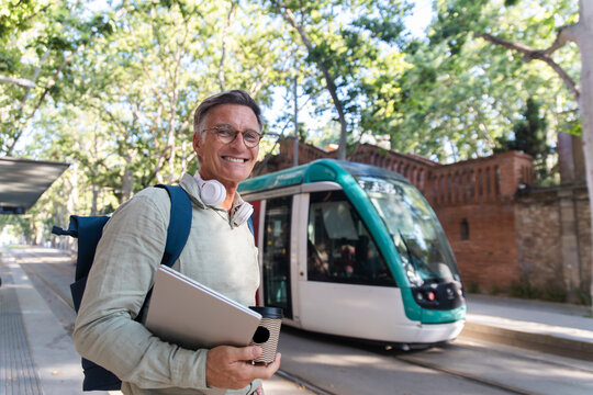 Smiling man holds laptop at a tram station in Barcelona Spain