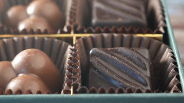 Panning shot of assorted luxury dark and milk chocolate pralines in elegant green gift box