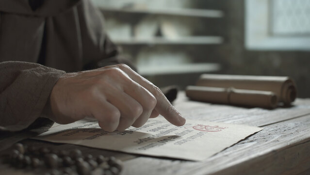 Scribe hands tracking words with a finger tip on a manuscript on a wooden table inside a medieval monastery scriptorium