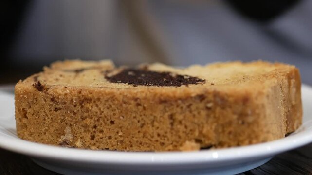 Close up of marble loaf cake on white plate with silver spoon taking small piece in cafe setting
