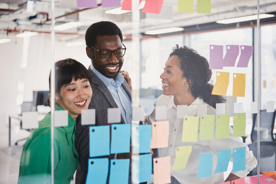 Business colleagues brainstorm with sticky notes on an office window