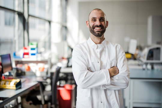 Smiling male scientist stands with arms crossed in a laboratory