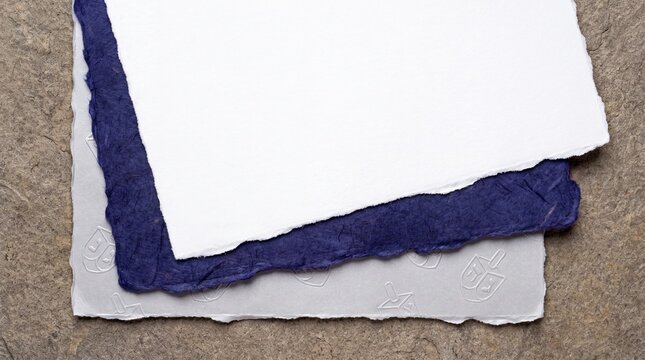 A textured surface showcases a stack of handmade paper, with one sheet in a deep indigo hue and another a crisp white, hinting at artisanal craft and creative potential.