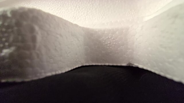 Close up footage of a molded white Styrofoam packaging container showing smooth curved edges and detailed cellular texture under warm ambient light. Great for product packaging themes