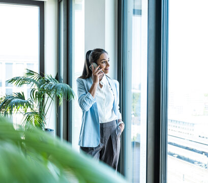 A businesswoman talks on a smartphone near an office window