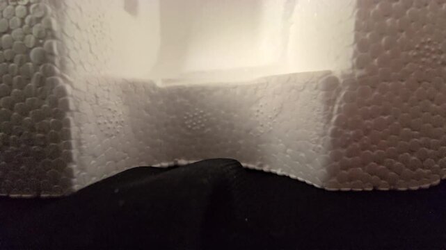 Close-up footage of a molded white styrofoam packaging container showing smooth curved edges and detailed cellular texture uder warm ambient light. Great for product packaging themes,