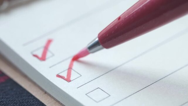 A close up view of a hand holding a red pen to mark checklist on paper creating a motion footage with selective focus and copy space for text