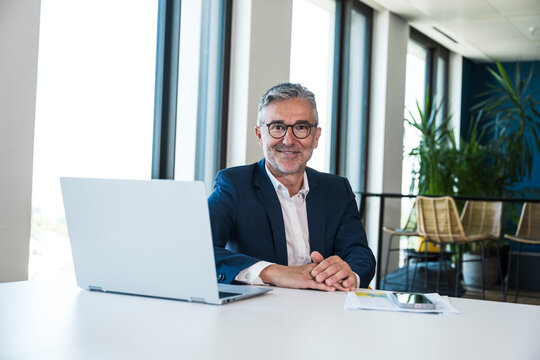 Smiling businessman works on laptop at the office desk