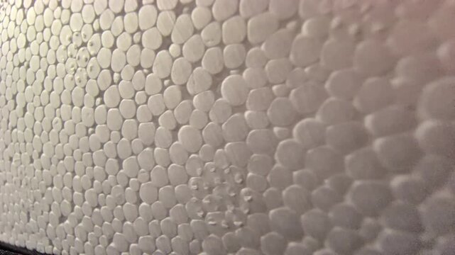 A close-up macro camera slow-pan over the detailed, bumpy surface of a white expanded polystyrene foam block, showing its unique cellular bead pattern under warm, soft lighting.