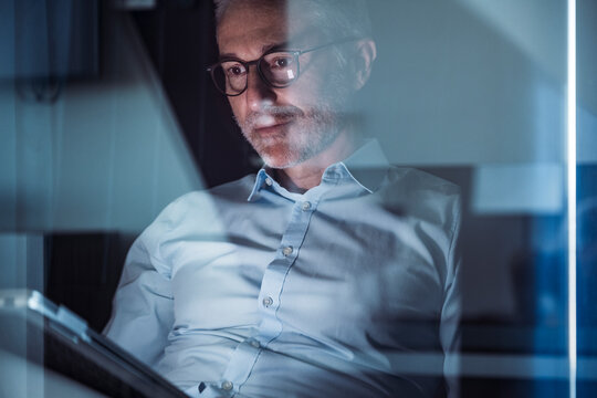 A businessman works on a tablet in a dark office at night