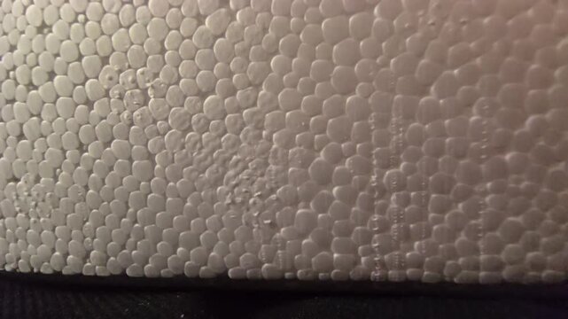 Detailed macro close-up of white polystyrene styrofoam texture featuring a soft warm lighting gradient and smooth cellular beads. Perfect for modern background overlays, material textures