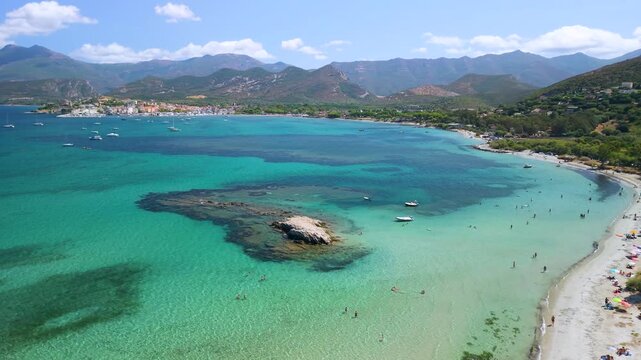 Saint-Florent Corsica drone flyover turquoise sea beach catamarans yachts town view bright sunny day, forward aerial flight over crystal clear water towards historic harbor Cinematic 4K aerial drone 