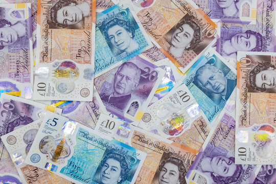 Heap of British pound banknotes with portraits of Queen Elizabeth II and King Charles III.