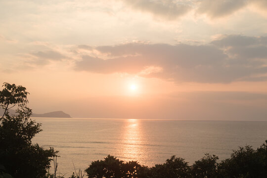 Sun setting over a calm sea with a glittering path of light and a distant cape, Amami Oshima, Japan