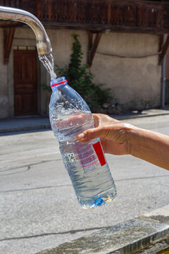 A hiker's hand is holding a pet bottle to refill the drinkable water from a public fountain in Switherland