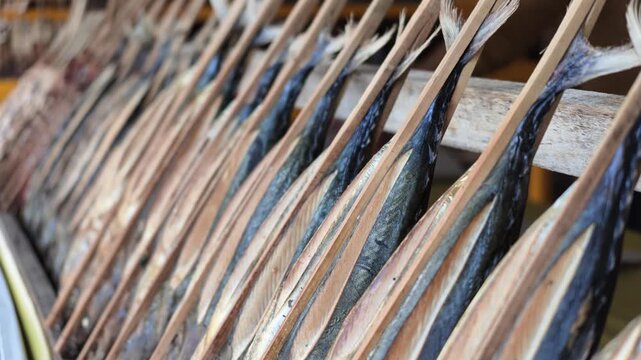 Tightly framed close-up showing rows of smoked fish tails bound on bamboo sticks, showcasing authentic coastal food preservation techniques.
