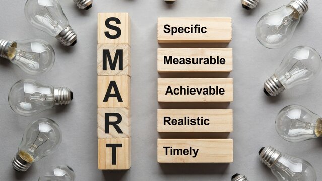 Wooden blocks with SMART acronym and text describing goal setting strategies surrounded by light bulbs. Business concept for planning and achieving objectives.