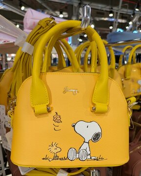 Tiempo de oto&ntilde;o. Bolso tote con cremallera, asas y correa de color amarillo, con Snoopy y Woodstock sentados, mientras cae una hoja de &aacute;rbol. Primark, Madrid, Espa&ntilde;a, 31 de julio de 2026