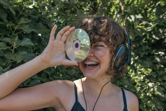 Teenage girl holds a CD and listens to music in a summer garden