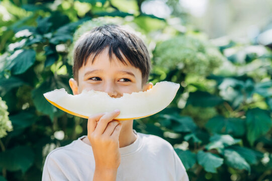 Boy holds a slice of melon like a smile outdoors