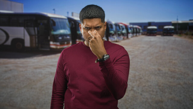 Man with beard in maroon sweater giving thumbs up gesture on a street lined with parked coaches and buses; confidence.
