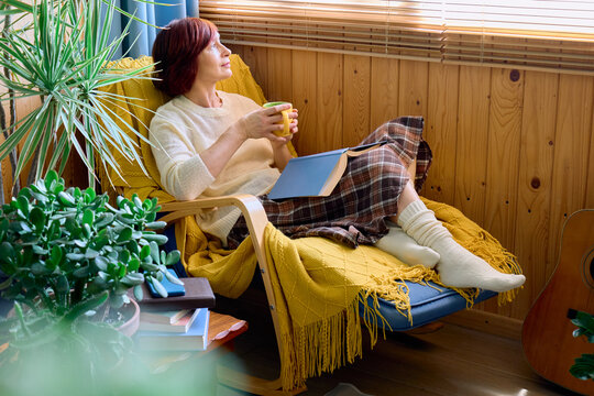 Woman relaxes in armchair with book and tea at home