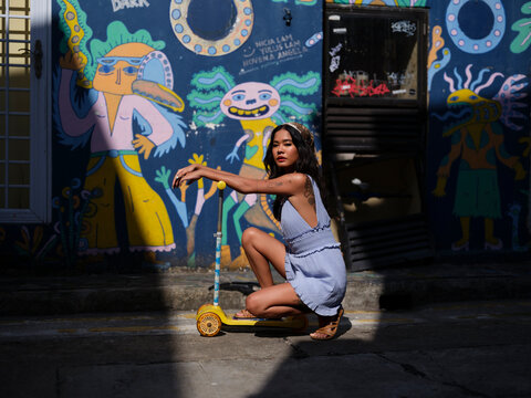 Woman crouches on a scooter by a colorful street art mural outdoors