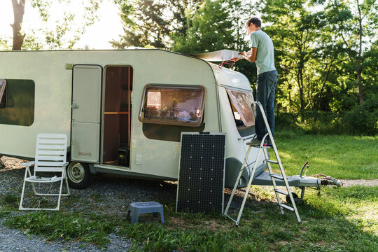 Man installs a solar panel on the roof of his camper at the campsite