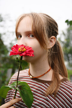 A young girl smells a red flower in a summer garden