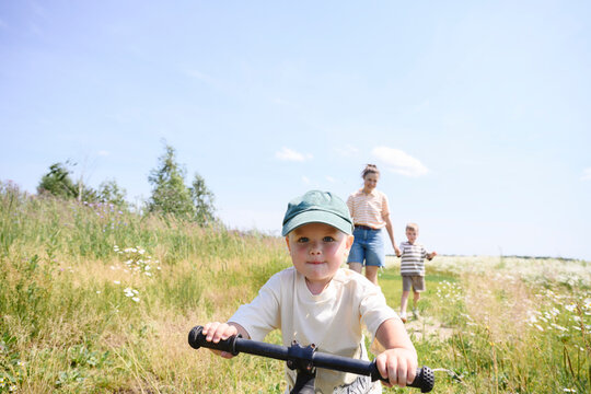 A young boy rides a bike while his mother and brother walk in a field