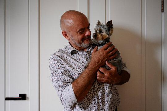 Mature man smiles and holds his Yorkshire terrier at home