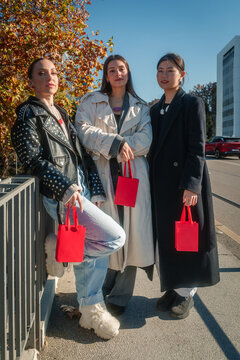 Fashionable women hold red shopping bags on an autumn city street