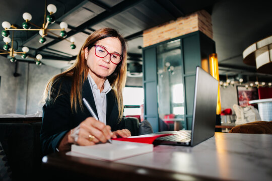 Businesswoman writing in notebook with laptop at hotel restaurant