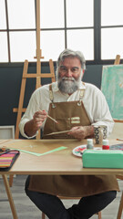 Man painter wearing apron holds a brush and paints paper at a table in studio with easel, palette and mug  quiet focus serenity. © Krakenimages.com