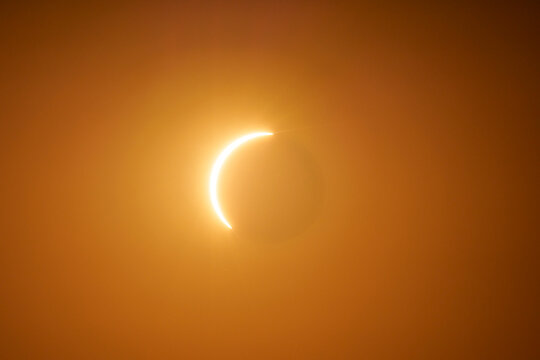 A total solar eclipse shows a glowing diamond ring in the orange sky