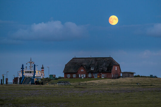Full moon over a thatched roof house and ferry at Rixwarf Germany