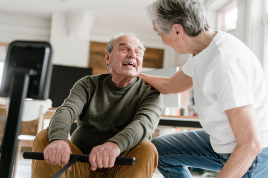 A female teacher supports a man on a rowing machine indoors
