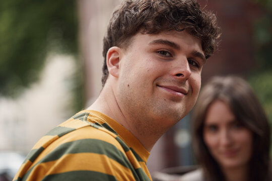 Smiling man looking at camera with female friend in background