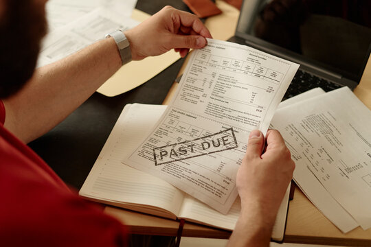 A man holds a past due bill at his workplace desk