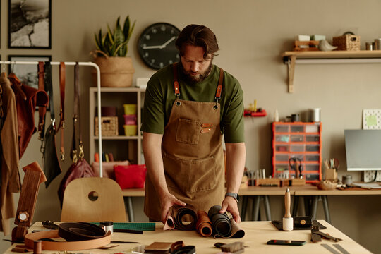 Male artisan working with leather rolls in his craft workshop