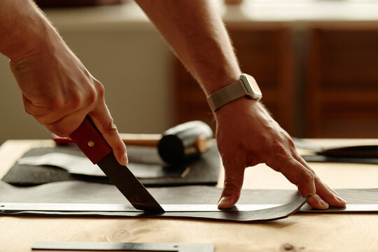 Male artisan cuts leather with a knife in the workshop