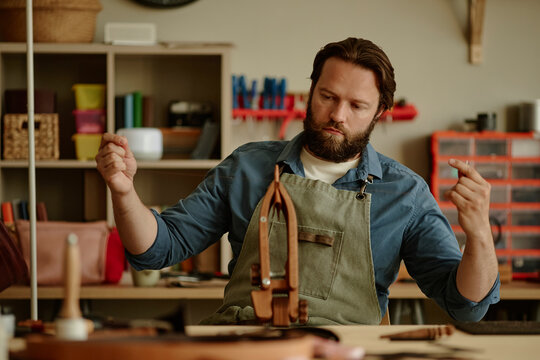 Male artisan sews leather at a workbench in his workshop
