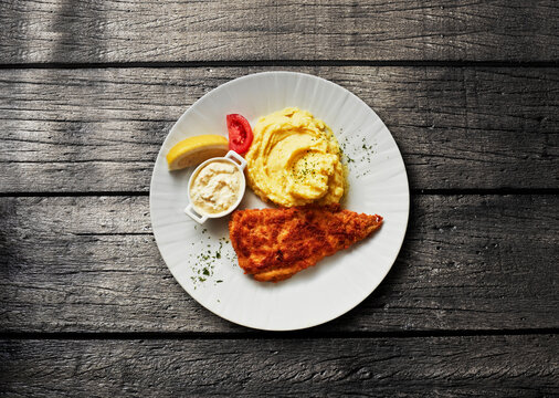 Breaded fish with mashed potato and remoulade on a wooden table