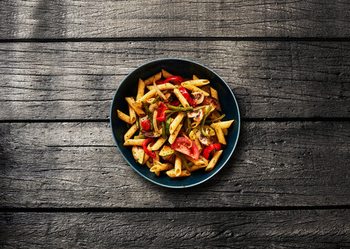 Bowl of vegetarian penne pasta with zucchini on rustic wooden table